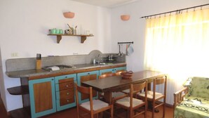 A compact kitchen with a dining area, featuring a wooden table and chairs, a small countertop, and a window with curtains. - Villa Paradisino Orbetello, Bilocale Flamingo B (Orbetello)