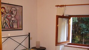 A bedroom with a bed, a nightstand, a window with a view of trees, and a painting on the wall. - Villa Paradisino Orbetello, Bilocale Flamingo B (Orbetello)