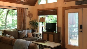 Una sala de estar acogedora con techo de madera, ventanas amplias, un sofá, una mesa de centro y un televisor.