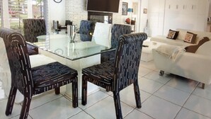 Ein modernes Wohnzimmer mit einem Glastisch, dunkel gemusterten Sesseln, einem weißen Sofa und einem flachbildfernseher an der Wand.