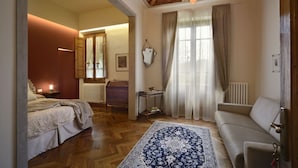 Quarto com cama, sofá, tapete estampado, lustre e janela com cortinas.