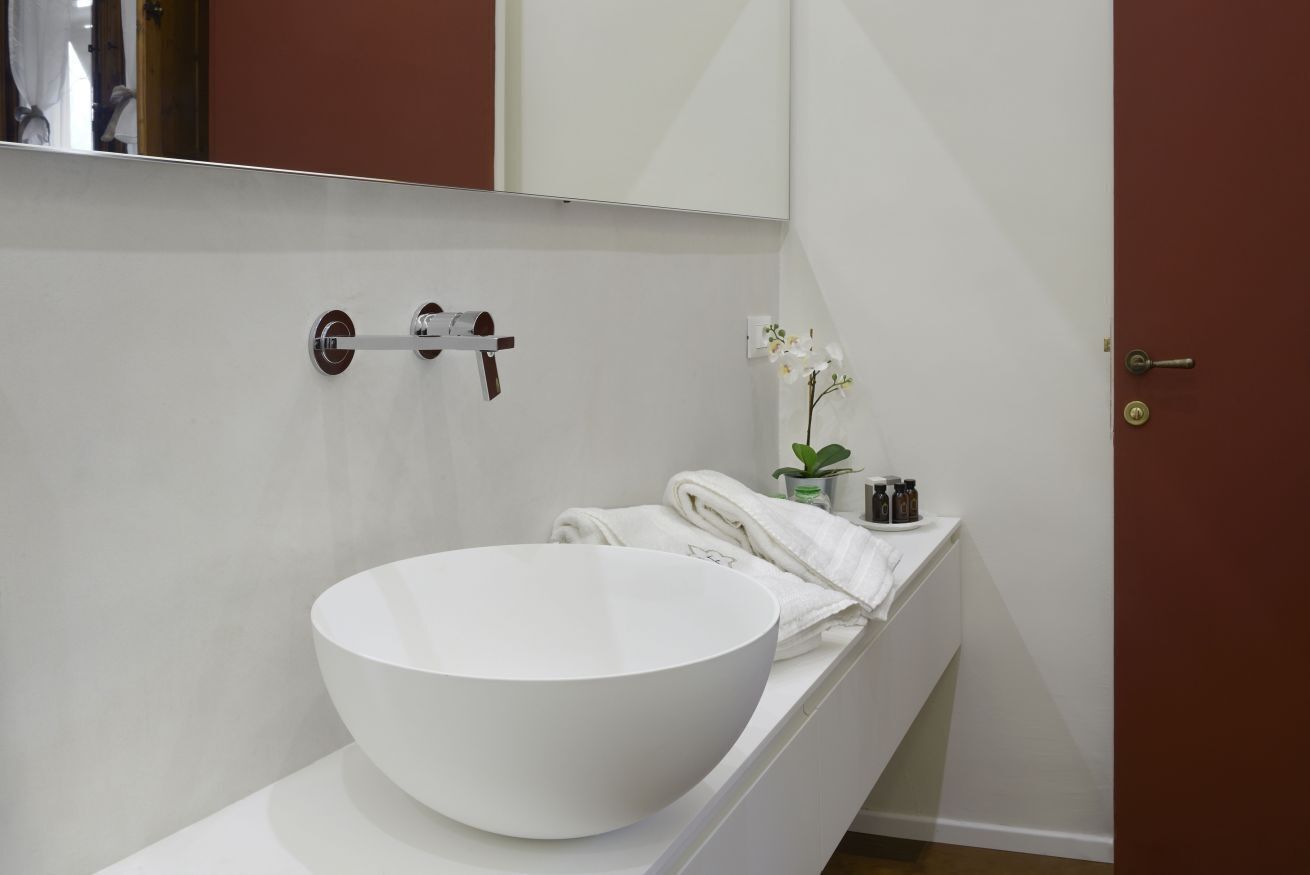 Un baño moderno con un lavamanos blanco de diseño, un perchero y una pequeña planta en maceta.