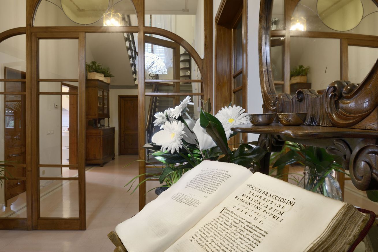An open book titled "POGGI BRACCHOLINI" on a table with a mirror and decorative items.