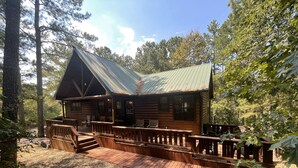 Une cabane rustique en rondins de bois, dotée d’une terrasse en bois et d’un toit de chaume.