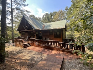 Surrounded by a natural forest, this cabin features a gabled roof and a cozy front porch with benches.
