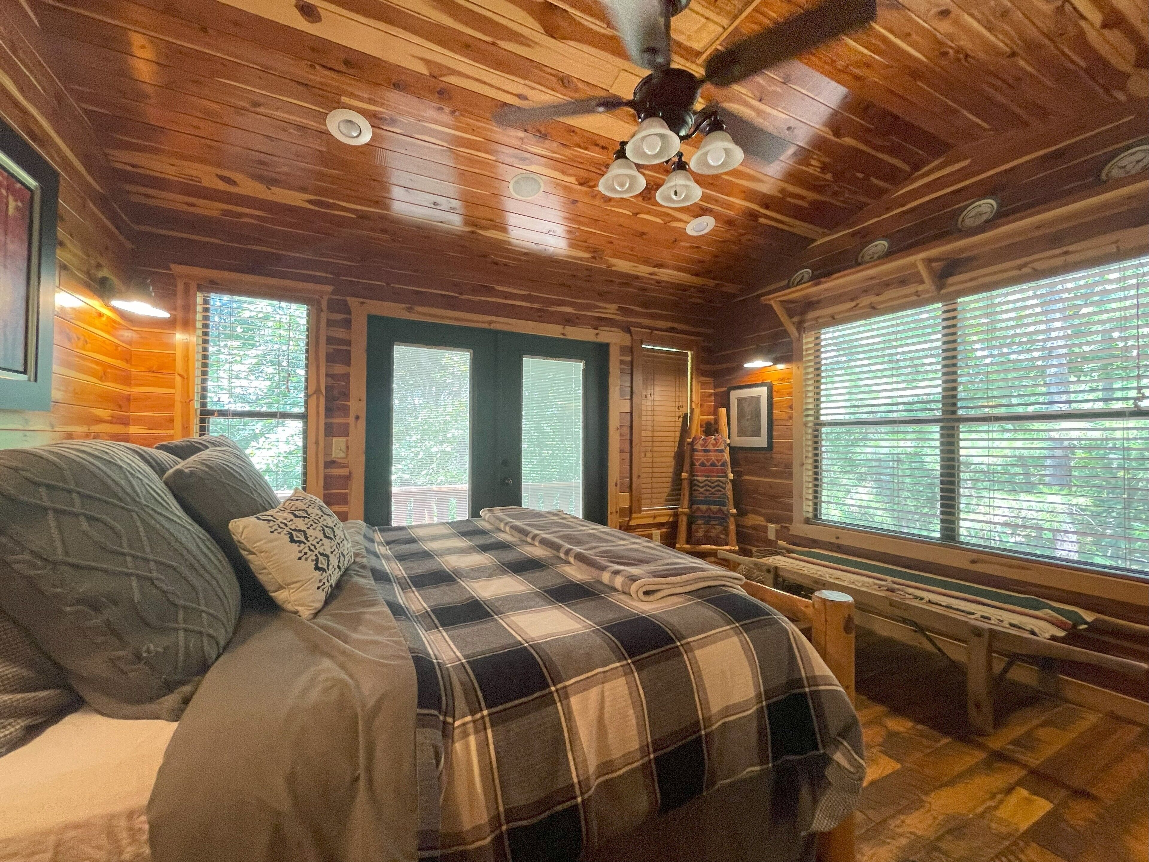 A cozy cabin bedroom with a bed, a bench, and a ceiling fan.