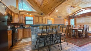 L’intérieur d’une cabine comprend un bar en pierre, des tabourets de bar en bois, un coin repas avec une table et des chaises, des meubles en bois et une grande fenêtre avec des stores.