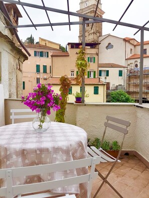 A balcony with a table and chairs, a vase with flowers, and a view of buildings in the background.