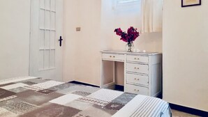 Ein Schlafzimmer mit Bett, Schminktisch, Fenster mit Vorhängen und einer Tür.