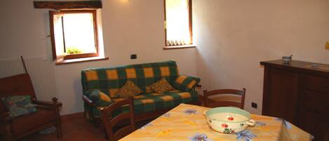 A cozy dining area with a table set for two, a green and yellow checkered sofa, wooden chairs, and a window with a view.