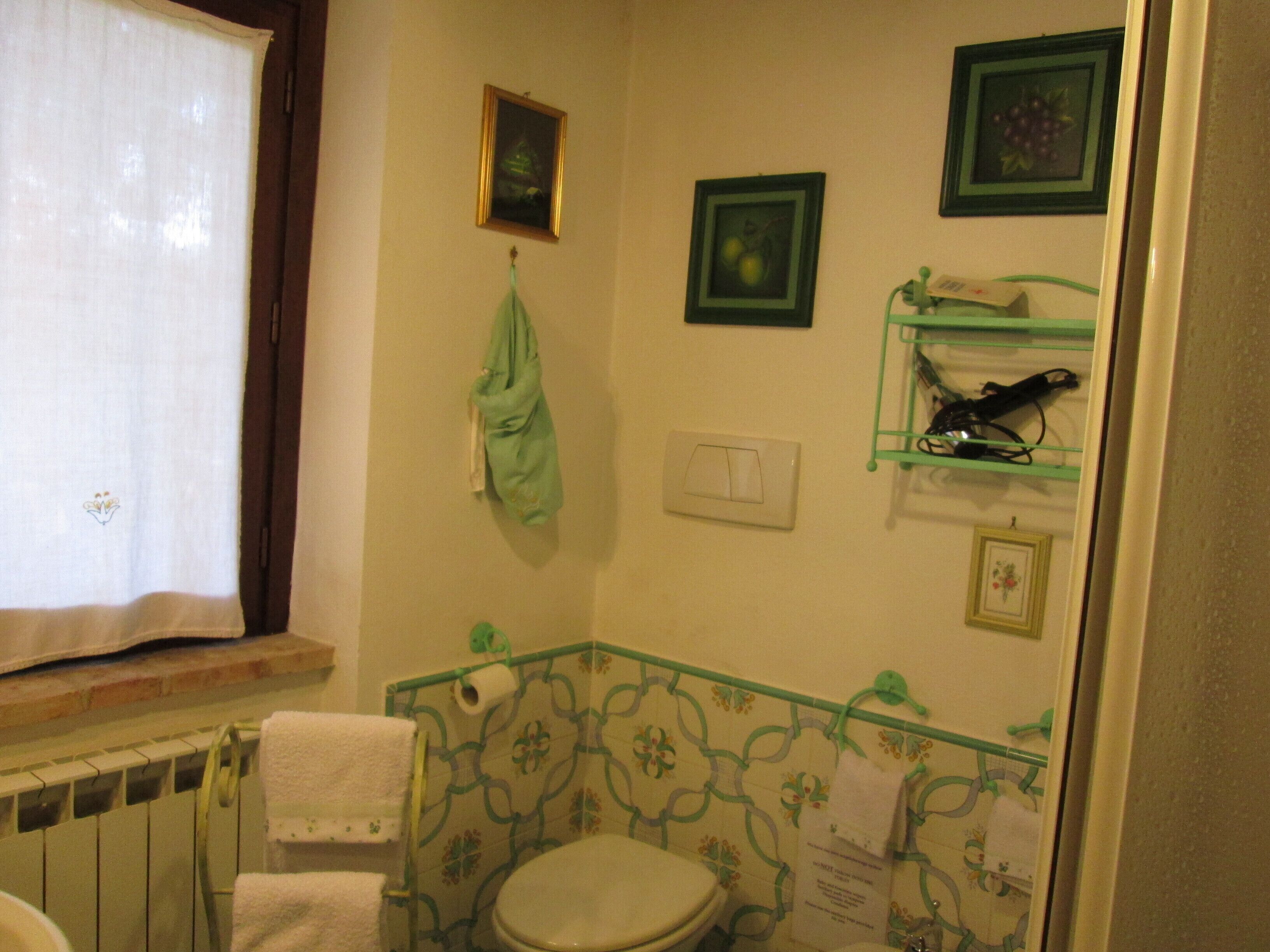 Un baño con inodoro, toallero, radiador y repisa con artículos de aseo.