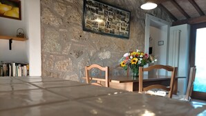 Un coin repas avec un mur en pierre, des chaises en bois, une table carrelée et un collage encadré accroché au mur.