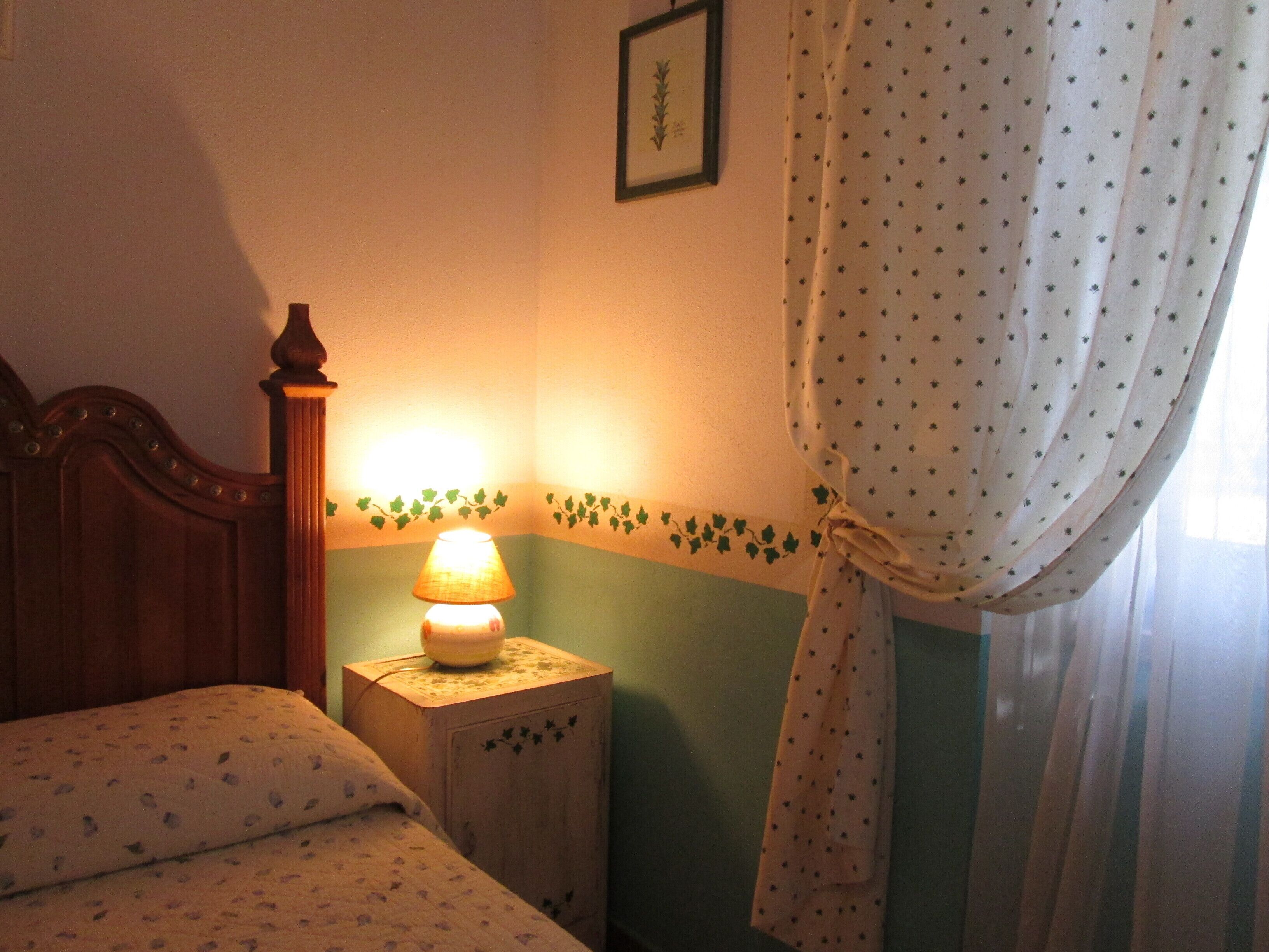 A bedroom with a wooden bed, a bedside table with a lamp, and a curtain.