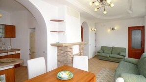 A living room with a green sofa, a wooden dining table with a plate, and a kitchen area with cabinets and a countertop. - RAVELLO "Nonna Anna" AMALFI COAST (RAVELLO)