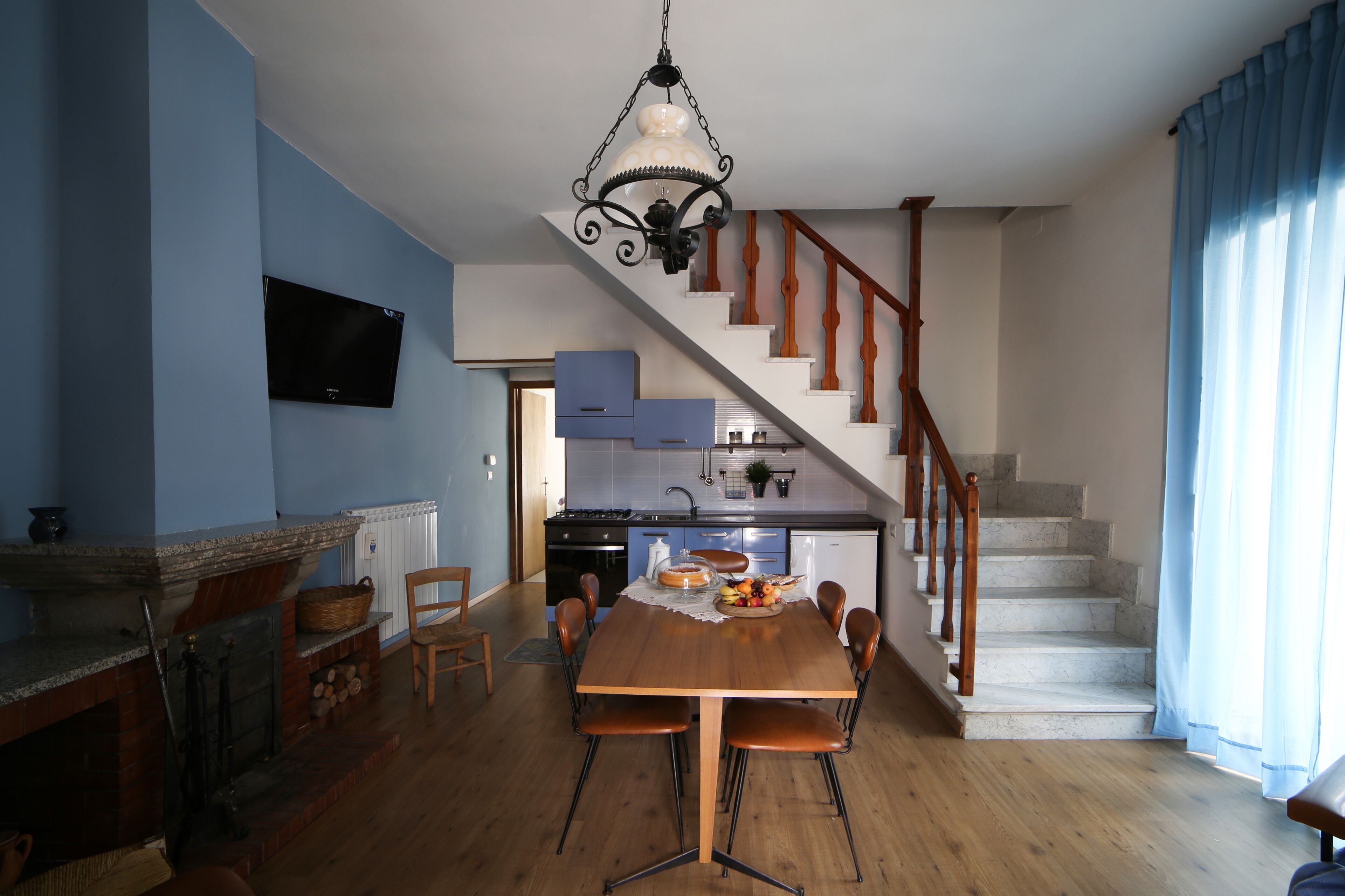 Un comedor con una mesa y sillas de madera, una chimenea y una cocina al fondo.
