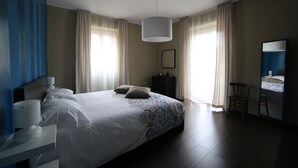 A hotel room with a large bed, a desk with a lamp, a chair, and a mirror. - "THE HOUSE OF THE VILLAGE" ....... (Brienza)