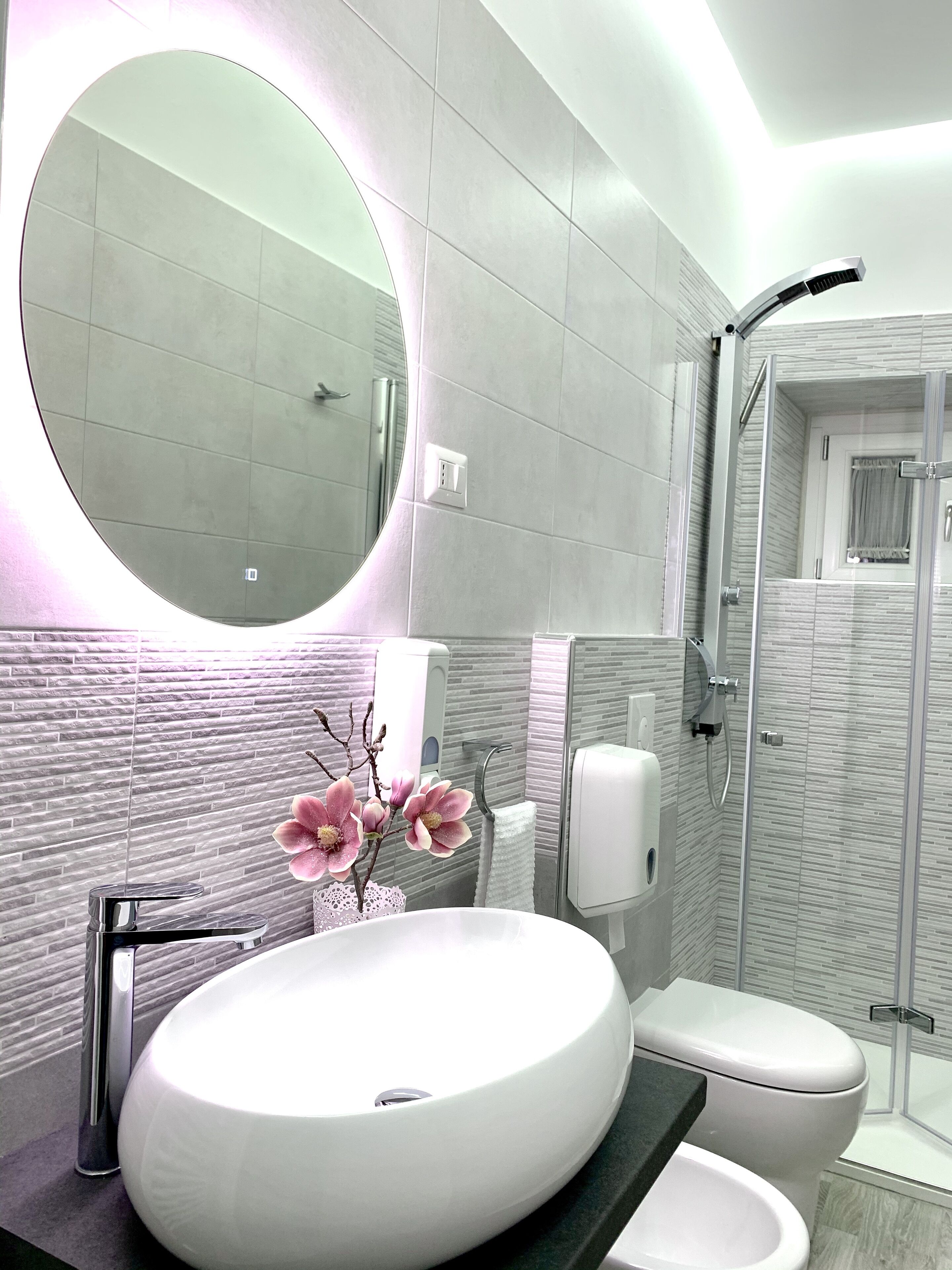 Een moderne badkamer met een grote ronde wastafel, een toilet, een douche en een spiegel.