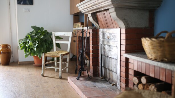 A rustic room with a brick fireplace, a wooden chair, a potted plant, and a wicker basket. - "THE HOUSE OF THE VILLAGE" ....... (Brienza)