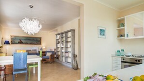 A dining area with a white table, blue and green chairs, a chandelier, and a bookshelf.