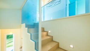 A modern interior with a staircase leading to an upper level, a door to the left, and a window on the upper floor.