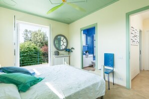 Quarto com cama, ventilador de teto, janela e porta para um banheiro.