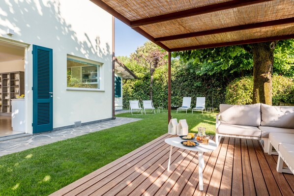 A modern outdoor patio with a wooden deck, a white sofa, and a table set with food and drinks.