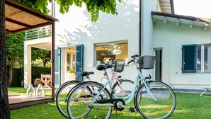 Two bicycles parked on a grassy lawn in front of a house with a covered porch.