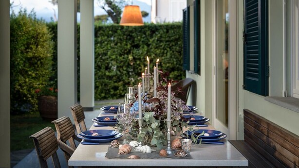 A table set for dining outdoors with candles, shells, and a floral centerpiece.