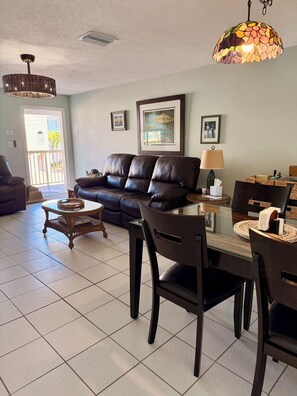 A living room with a leather sofa, a glass coffee table, and a dining table with chairs.