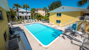 A rectangular swimming pool with a white border, surrounded by lounge chairs and a small table.