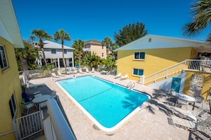 A rectangular swimming pool with a white border, surrounded by lounge chairs and a small table.