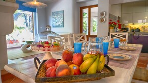 Uma mesa de pequeno-almoço com frutas, um bolo em cúpula de vidro e chávenas azuis.