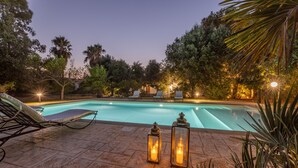 Uma piscina com espreguiçadeiras e lanternas, cercada por árvores e um espaço de estar ao ar livre.