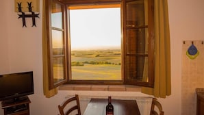 Un comedor con una mesa, sillas, una botella de vino y vistas a través de un ventanal abierto.