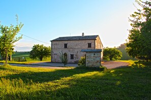 Un edificio in pietra con tetto spiovente, circondato da vegetazione lussureggiante e un cielo sereno.