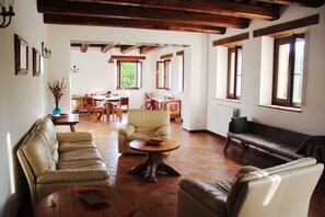 Un'ampia zona giorno con un divano, un tavolino rotondo in legno e una panca. Sullo sfondo, un'area pranzo con tavolo e sedie.