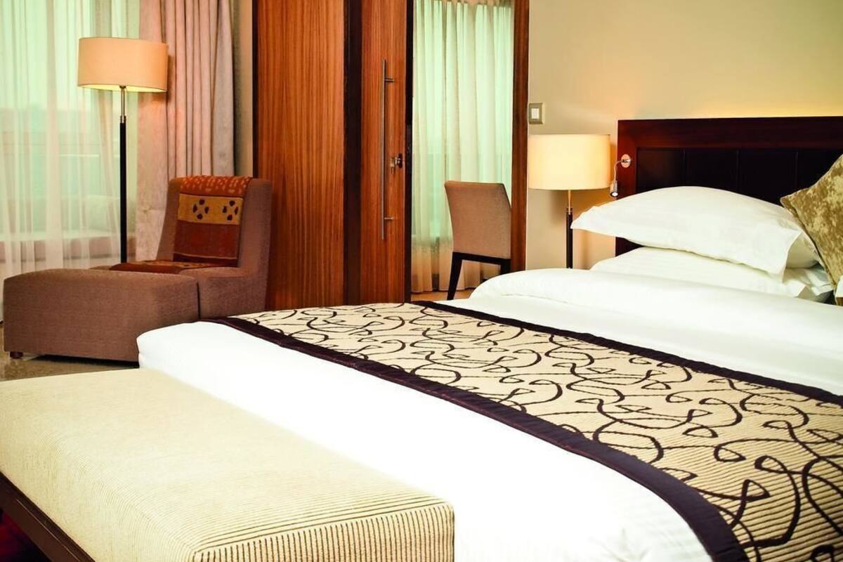 A hotel room with a bed, a chair, a sofa, and a lamp.
