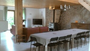 A dining area with a long table and chairs, a television, and a stone wall. - The Pyrenees footbridge (Unac)
