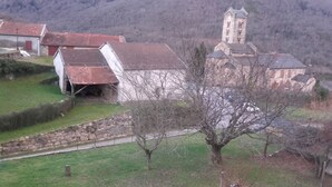 A rural village with stone walls, a church with a bell tower, and traditional houses with red roofs. - The Pyrenees footbridge (Unac)