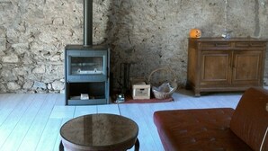 A rustic room with a stone wall, a wooden cabinet, a sofa, and a wood-burning stove. - The Pyrenees footbridge (Unac)
