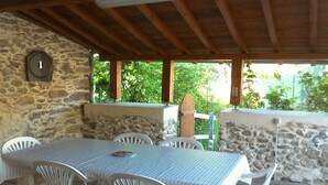 An outdoor patio with a stone wall, a wooden ceiling, and a table with chairs. - The Pyrenees footbridge (Unac)