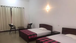 A hotel room with two beds, a desk, a chair, and a window with curtains. - Canalside Villa & Guest House (Ginigathena)