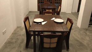 A dining area with a wooden table and chairs, a set of plates, and cutlery. - Canalside Villa & Guest House (Ginigathena)