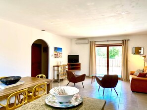 Uma sala de estar com área de jantar, TV e varanda com cortinas.