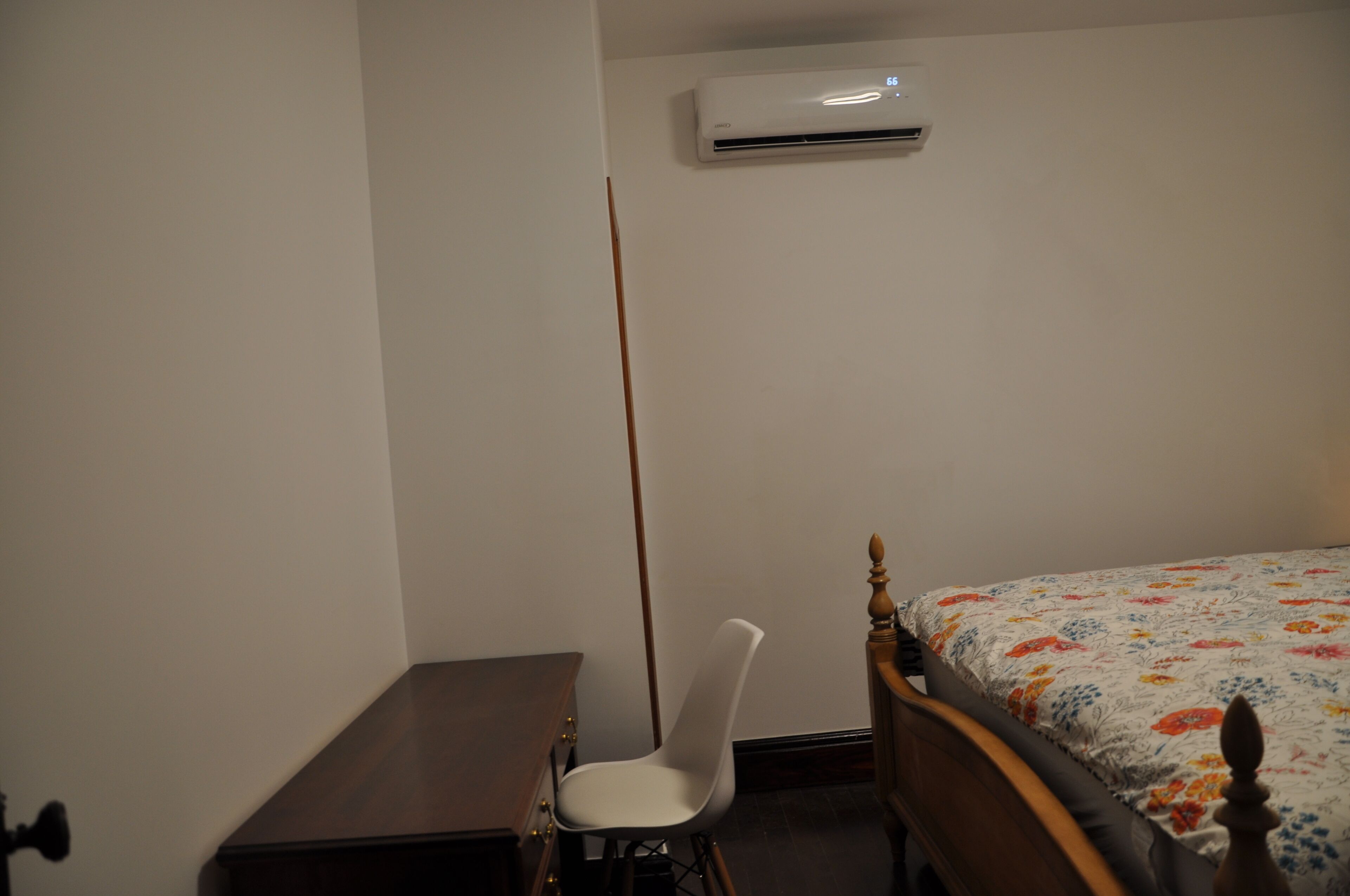 A bedroom with a wooden bed, a desk, a chair, and an air conditioning unit on the wall.
