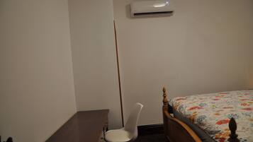 A bedroom with a wooden bed, a desk, a chair, and an air conditioning unit on the wall.