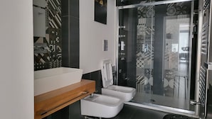 Une salle de bain moderne avec un grand miroir, deux toilettes, une douche et un lavabo.