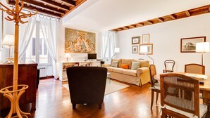 Un vaste salon doté d’un parquet en bois, d’un fauteuil noir, d’un canapé et d’un coin repas avec une table et des chaises.