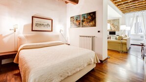 Une chambre avec un grand lit, un plancher en bois, des murs blancs et des œuvres d’art.
