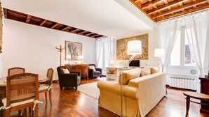 Un salon spacieux doté d’un parquet, d’un canapé, d’une table à manger avec des chaises, d’un lampadaire et d’un tableau accroché au mur.